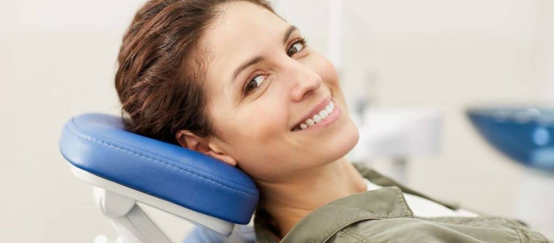bleeding-gums A woman smiles while reclining in a dental chair at Dental Grande Prairie, looking at the camera.