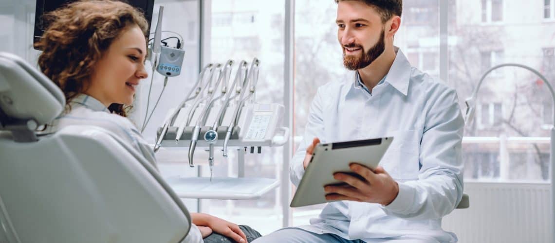 A dentist at a modern dental grande prairie clinic shows a tablet to a female patient, with advanced dental equipment visible in the background.