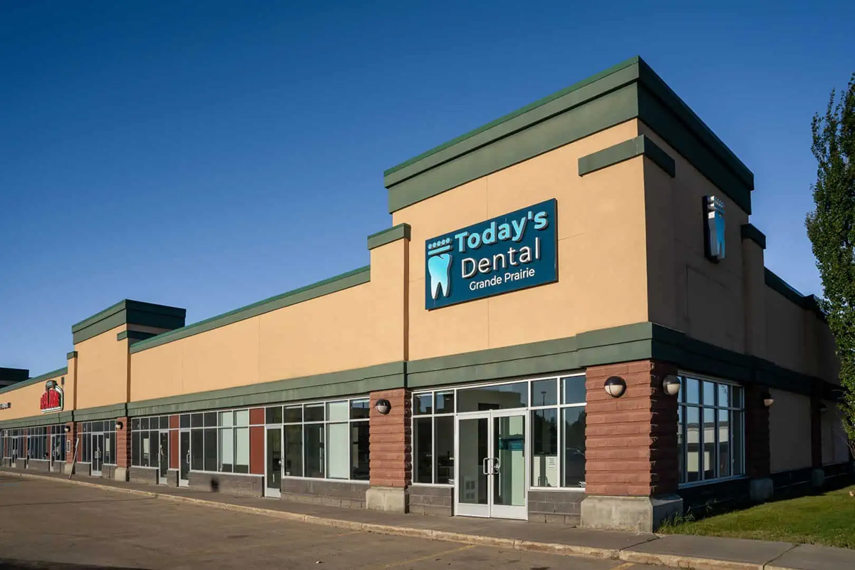 A beige and green commercial building with large windows houses Today's Dental Grande Prairie, a trusted dental clinic serving the local community.