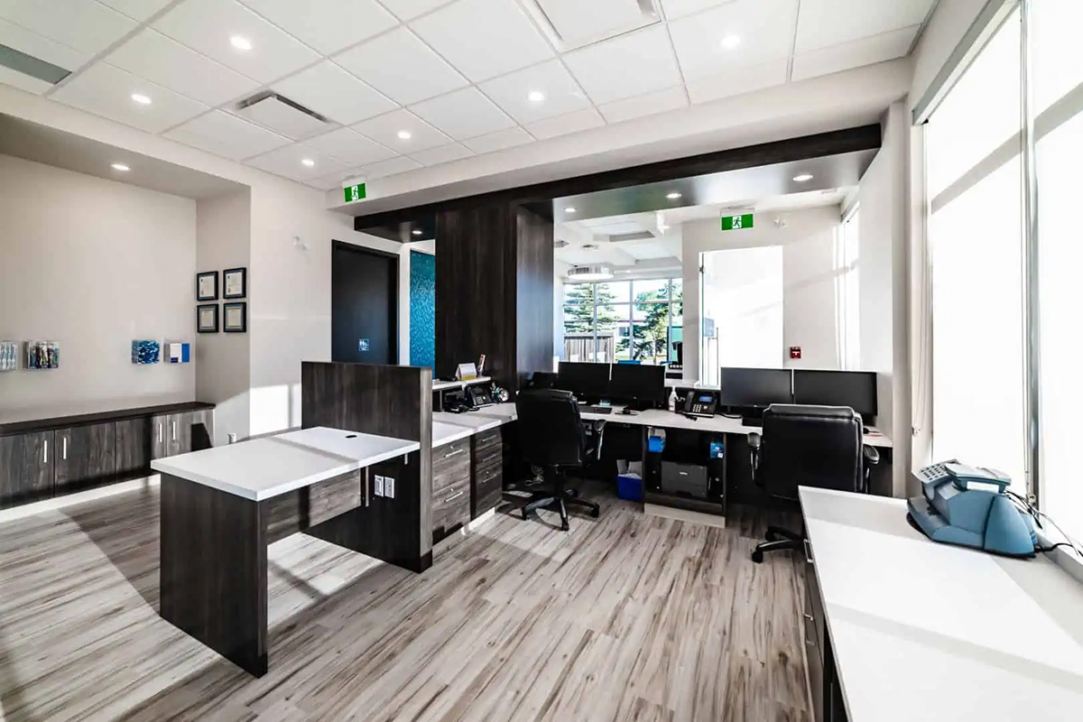 Modern office space with multiple desks, office chairs, computer monitors, and large windows allowing natural light into the room—ideal for a dental Grande Prairie team seeking a bright and comfortable work environment.