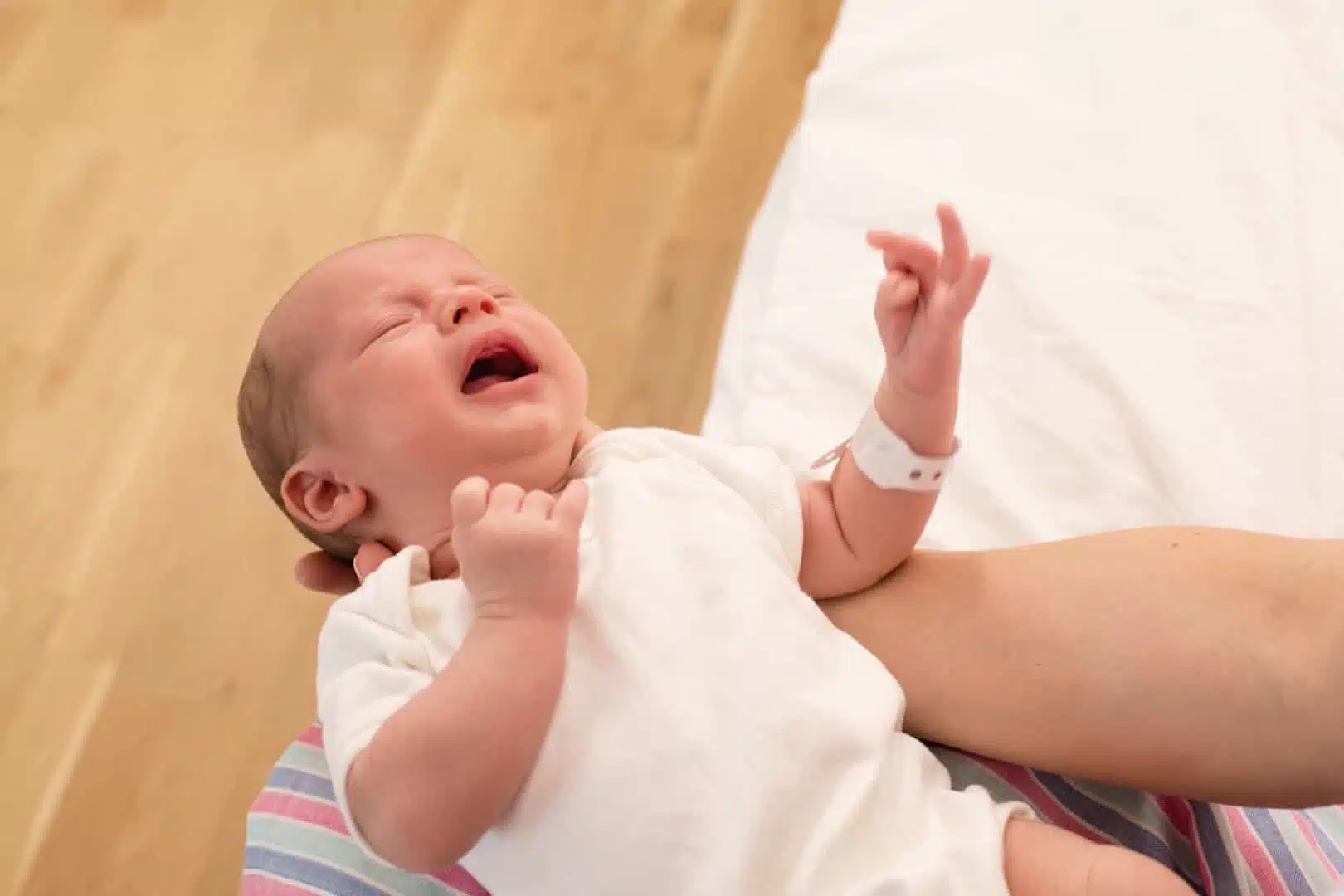 tongue-lip-ties-featured-image A newborn baby wearing a white onesie and hospital wristband is crying while being held in someone's arms at a hospital near dental Grande Prairie.
