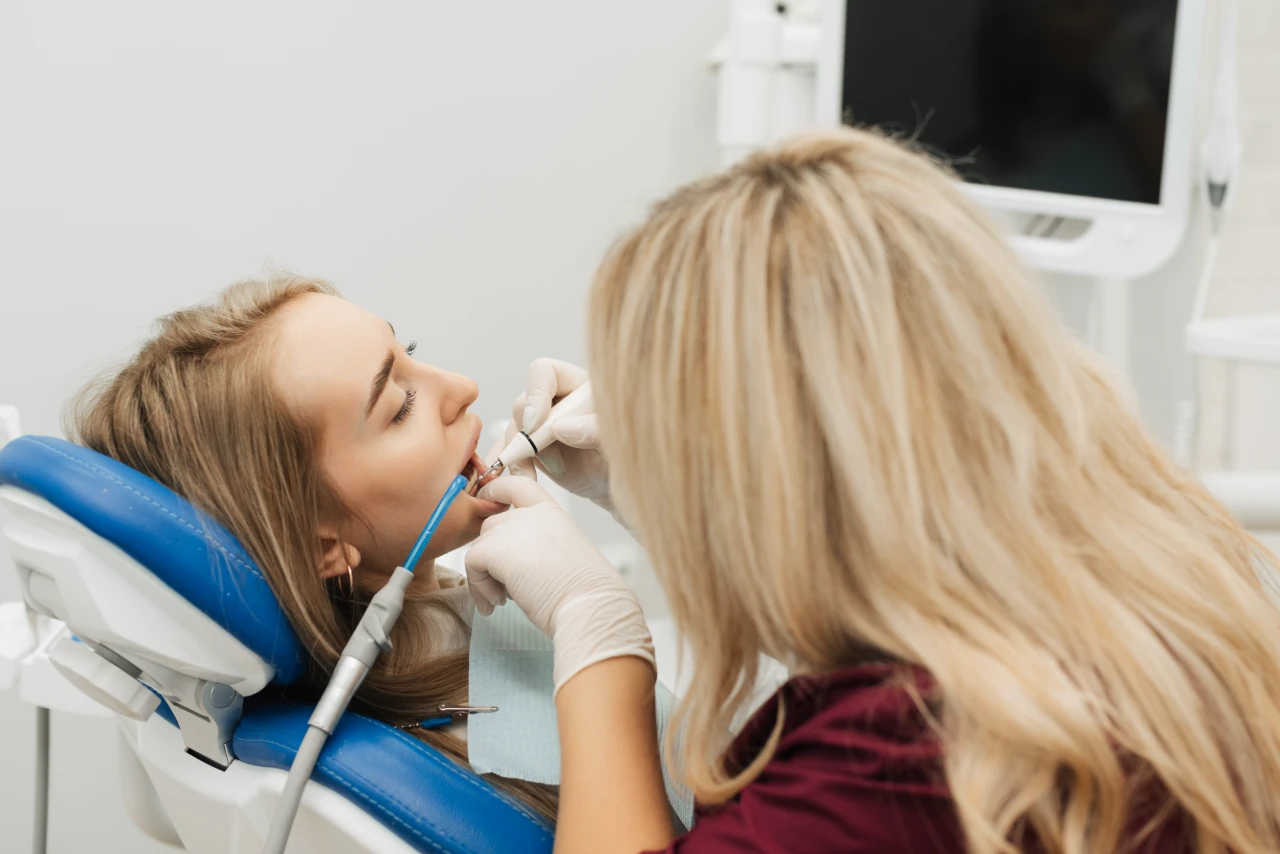 A dentist wearing gloves performs a dental procedure on a patient lying in a dental chair, using dental instruments.