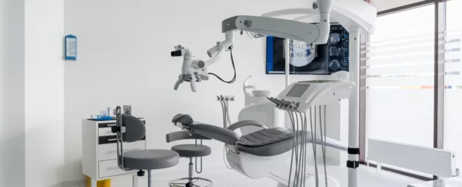 A modern dental clinic room with an empty dental chair, overhead light, dental instruments, and medical equipment in a bright, clean setting.