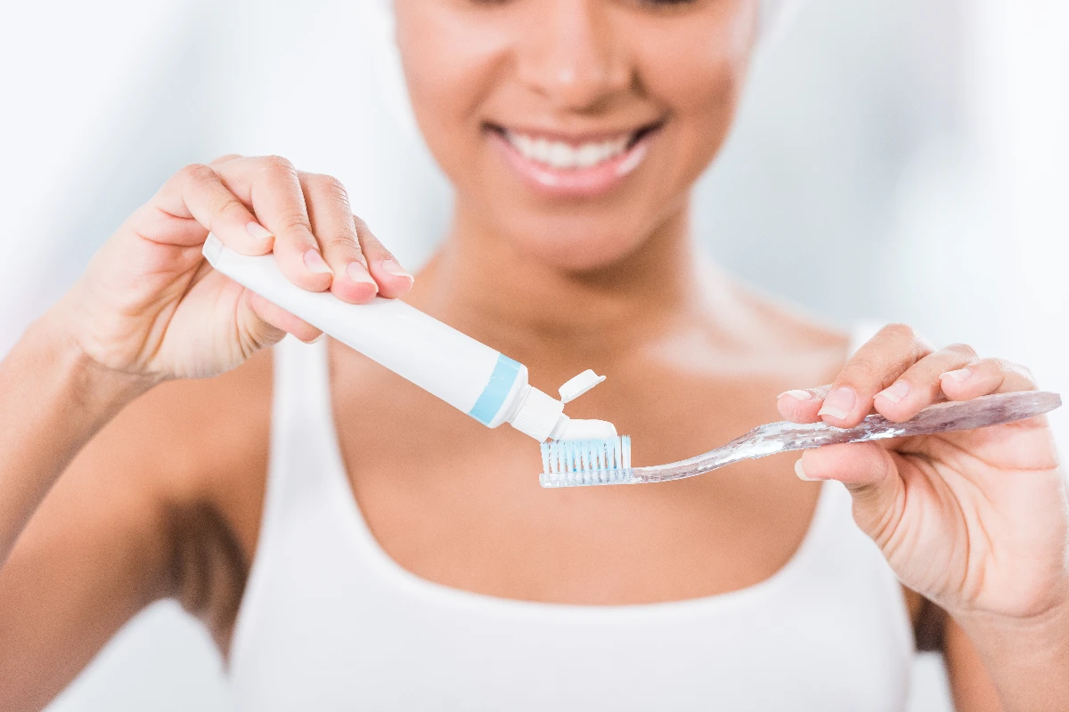 A person smiling while squeezing toothpaste onto a toothbrush.